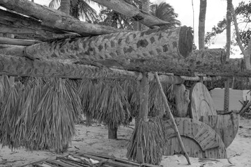 Black and white photo of a traditional beach hut structure made from wood and palm leaves, with a rustic appearance.