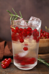 Refreshing water with red currants and rosemary in glass on wooden table, closeup
