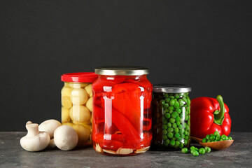 Different pickled products in jars on grey textured table