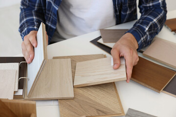 Man choosing wooden flooring among different samples at table, closeup