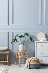 Stylish interior with stool and chest of drawers near light grey wall