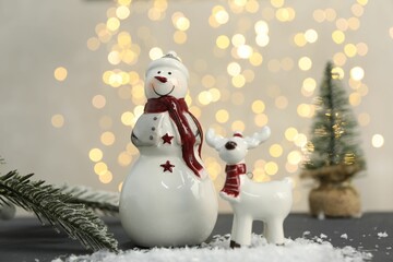 Funny snowman figure and decorative reindeer on table against blurred lights