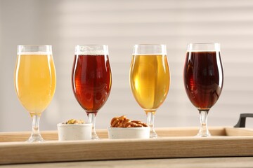 Glasses with different types of beer and snacks on wooden table indoors
