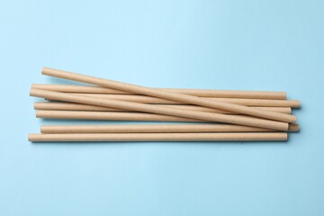 Bamboo drinking straws on light blue background, top view
