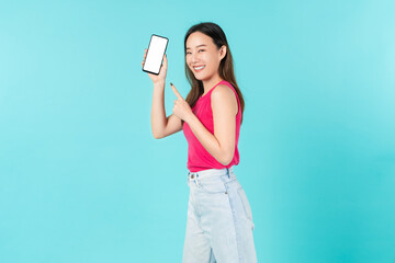 Beautiful Asian woman pointing finger on mobile and holding smartphone mockup of blank screen on blue background.