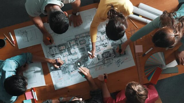 Top down view of civil engineer team writing at blueprint at meeting table with color palettes. Group of diverse people planning and taking a note while manager looking at project plans. Symposium.