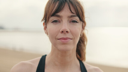 Mindful happy girl outdoors standing on the seafront and smiling, active lifestyle. Attractive young woman looking at camera