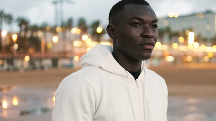Fototapeta premium A highly motivated athlete in white hoodie prepares for street workout against the background of city lights and sea, sports motivation, active lifestyle