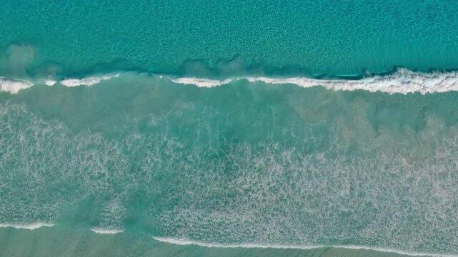 Waves crash on the shore with crystal clear blue waters over white silica sand in Esperance Australia