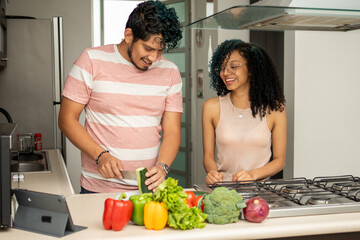 young adult couple cooking at home, indoors, cutting vegetables and preparing ingredients for a healthy salad