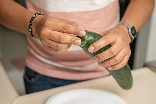 close up on hands of a young man rubbing cucumber ends to reduce bitterness; Hispanic person making a salad slicing ingredients