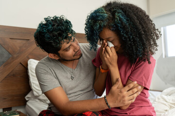 Concerned Hispanic husband offering emotional support to his distressed wife. Sad African American woman facing relationship challenges, sitting on the bed at home