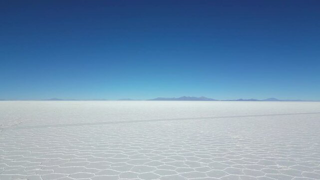 Drone shot of the immense Salar de Uyuni salt flat, the largest in the world, taking off from the salt bed where the typical hexagons are visible and gaining altitude revealing the never ending view