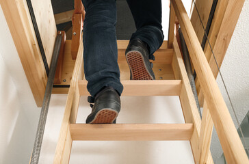 Back view of person using loft ladder or attic ladder. Woman climbing or going up loft sliding...