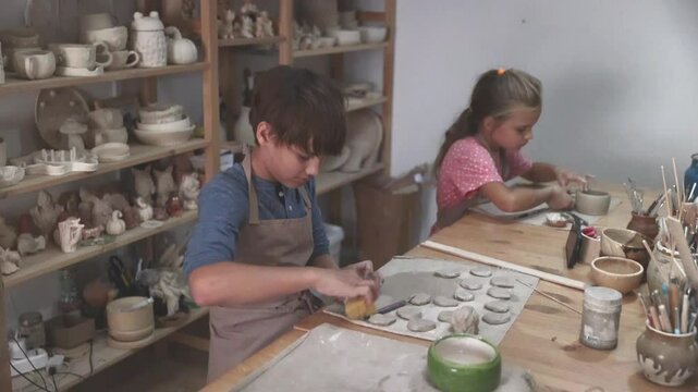 kids works with clay makes  ceramic plate in pottery school.  Children arts a crafts class in workshop.  the child sculpts from clay.