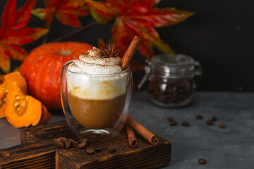 A glass of autumn pumpkin latte with whipped cream and spices. Coffee with pumpkin and cinnamon on a dark background