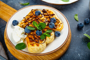Homemade waffles with blueberries, chocolate sauce and cream cheese in a plate