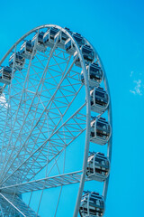 A close-up view of a modern Ferris wheel against a bright blue sky at an amusement park during daytime