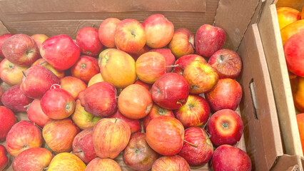 A box of apples is piled high with red and green apples. The apples are shiny and fresh, and they are arranged in a way that makes them look like a colorful and inviting display