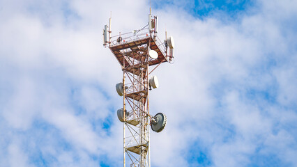 A tall tower with a lot of antennas on top. The sky is blue with some clouds. The tower is a cell...