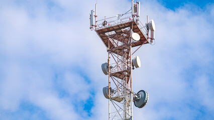 A tall tower with many antennas on top. The sky is blue and there are some clouds. The tower is a...