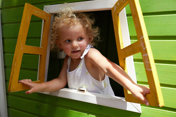 A young girl leans out of a playground cubby house window at something that caught her eye to the right