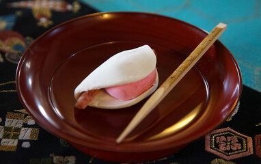 White and pink mochi sweets called Japan sakura mochi on a plate and wooden skewers