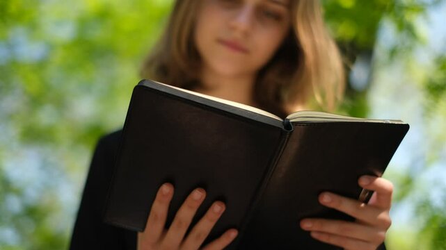 young woman student reading a book in the park on a bench on a sunny summer day
