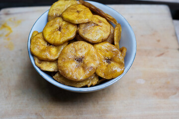 Keripik pisang or banana crackers on a white bowl at wooden cutting board. With copy space. Indonesian traditional snack made from banana and sugar.