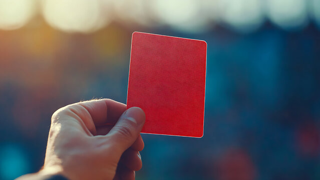 A hand holds a red card, likely a sports penalty card. Blurred background
