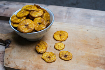Keripik pisang or banana crackers on a white bowl at wooden cutting board. With copy space. Indonesian traditional snack made from banana and sugar.