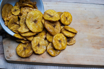 Keripik pisang or banana crackers on a white bowl at wooden cutting board. With copy space. Indonesian traditional snack made from banana and sugar.
