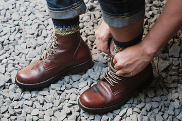 Man is putting on a pair of brown full grain leather shoes boots at outdoor with stone floor, Trying shoes leather boots.