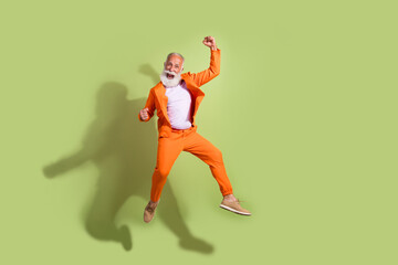 Full length photo of funny showman jump raise fists wear orange suit isolated on green color...