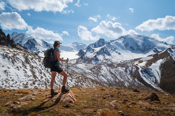 A girl with a backpack on a hike standing on a rock looking at the mountains. 