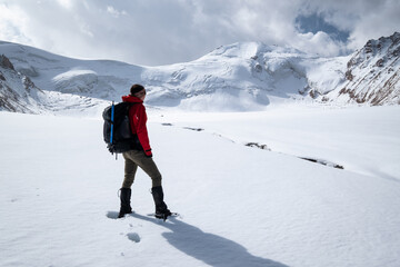 A woman with a backpack standing on a glacier looking at the top of a mountain in Kazakhstan