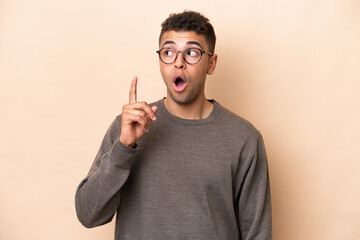 Fototapeta premium Young Brazilian man isolated on beige background thinking an idea pointing the finger up