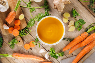 Top view of a bowl of vegetable soup with carrots, herbs, and ginger on a wooden background. Perfect for healthy eating and seasonal meal concepts