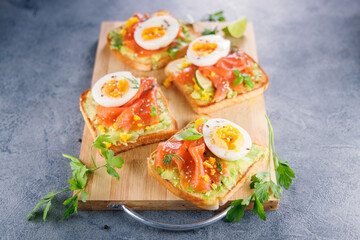 Avocado, smoked salmon, and egg on toast served on a wooden board. Perfect for healthy breakfasts and gourmet meals