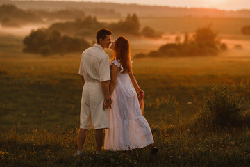 A couple in love in white clothes in a field at a red sunset