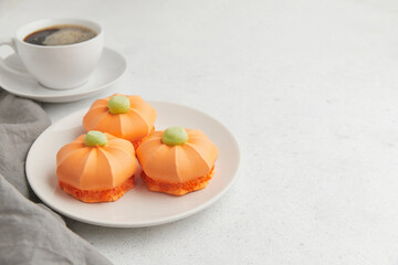 Three pumpkin shaped desserts with green tops on a plate, accompanied by a cup of coffee