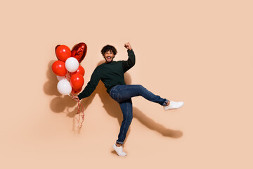 Full length photo of lucky handsome guy wear sweatshirt rising fist holding balloons emtpy space isolated beige color background