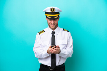 Airplane caucasian pilot isolated on blue background sending a message with the mobile