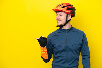 Young cyclist caucasian man isolated on yellow background pointing to the side to present a product