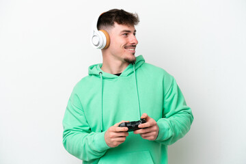 Young handsome man playing with a video game controller isolated on white background looking to the side and smiling