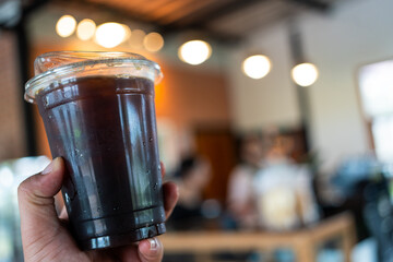 Hand of man holding a take out iced black coffee at coffee shop