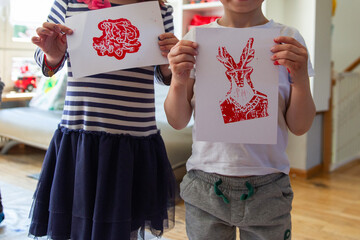 Children creating lino cut prints on paper using rollers, paint, and spoons in an art workshop. Creativity, craft techniques, and artistic expression, educational and creative stock imagery.