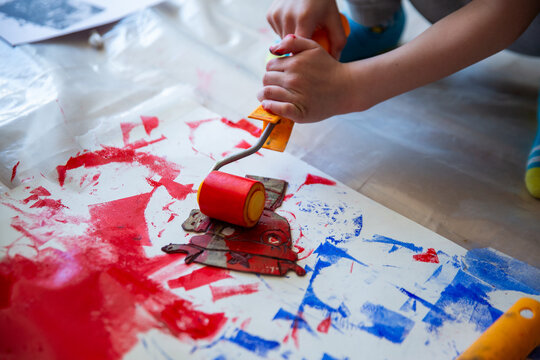 Children creating lino cut prints on paper using rollers, paint, and spoons in an art workshop. Creativity, craft techniques, and artistic expression, educational and creative stock imagery.