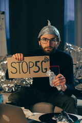Stop 5G! A man in a foil cap holds a sign and a phone wrapped in foil.