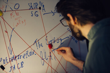 A man is standing near a crazy table on a conspiracy theory board.